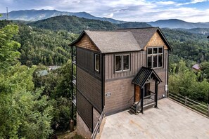 En træhytte med balkon, omgivet af skov og bjerge.