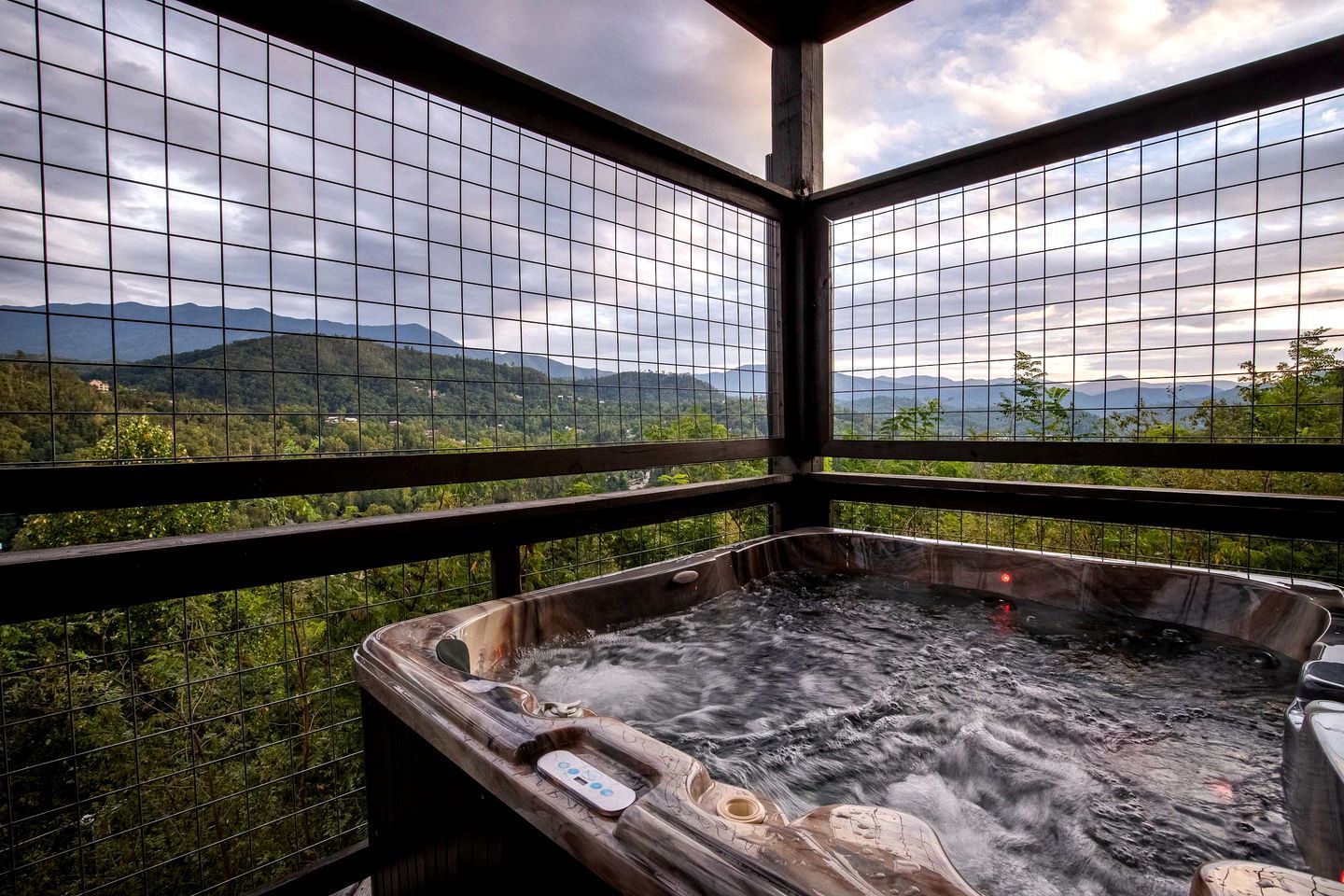 Een jacuzzi met houten rand en uitzicht op bergen door een raamrooster.