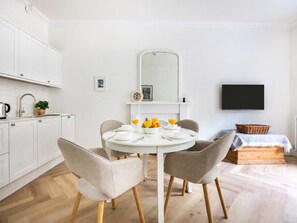 Eine moderne Küche mit weißen Schränken, einem runden Esstisch mit zwei Stühlen und einem an der Wand montierten Flachbildfernseher.