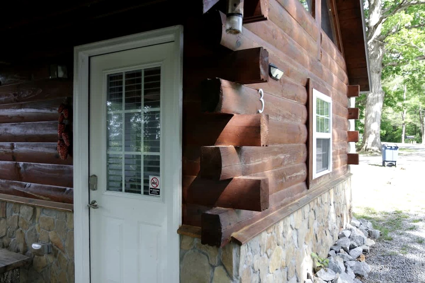 Eine Blockhütte mit Steinuntergrund, einer weißen Tür und zwei Fenstern mit Fensterläden.