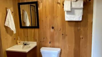 A wooden-paneled bathroom with a toilet, sink, mirror, and hanging towels.