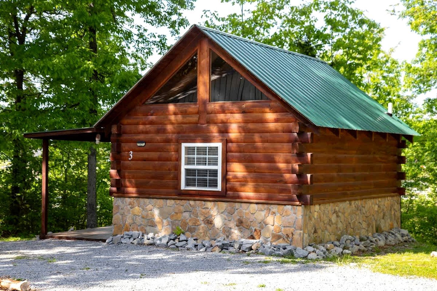 A log cabin with a stone foundation, a green metal roof, and a small window.
