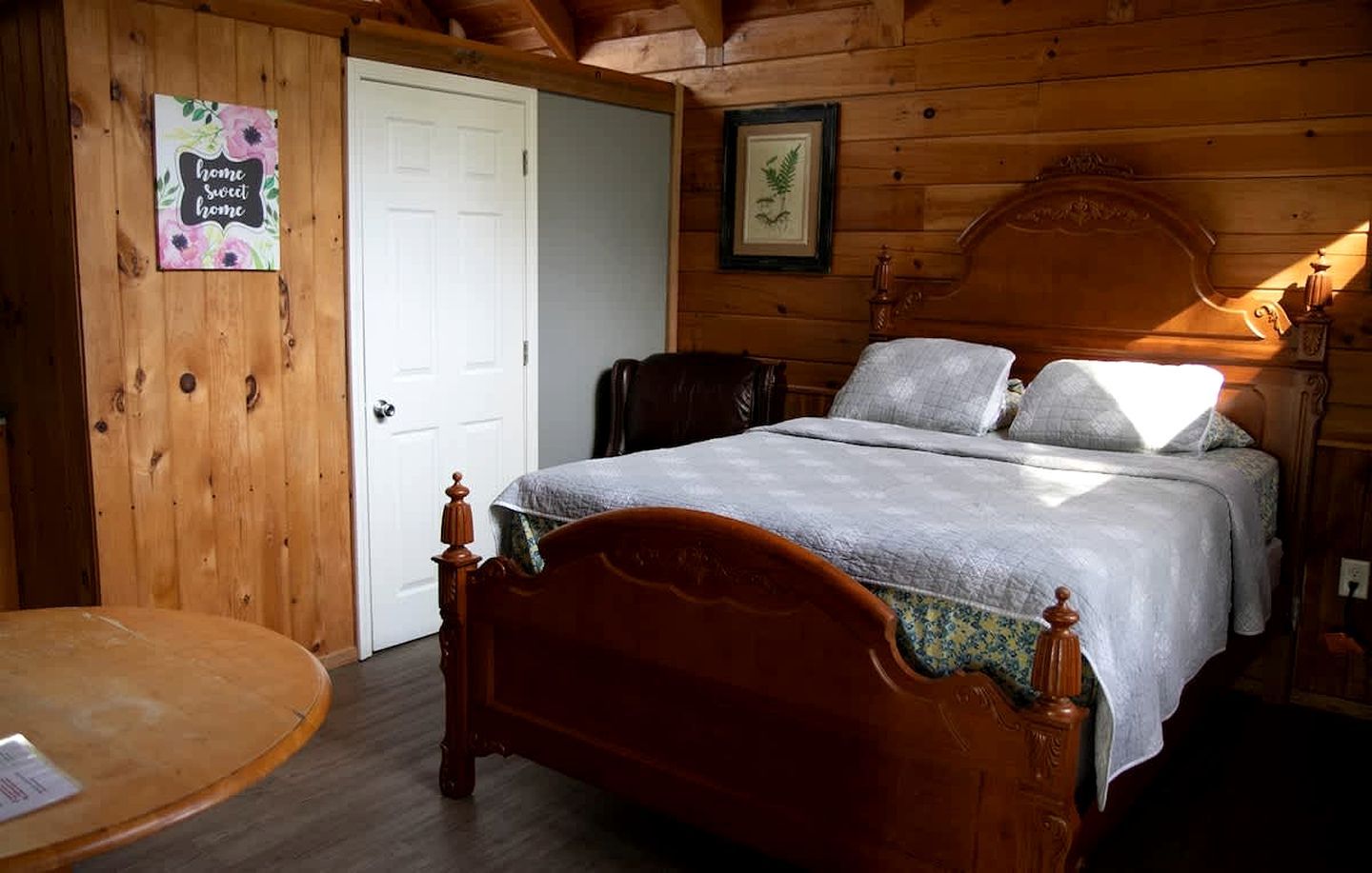 A wooden room with a bed, a chair, a small table, and a door.