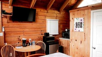 Ein Holzblockhaus-Interieur mit Essbereich, einem an der Wand montierten Fernseher, einer Küchenzeile mit Geräten und einer Tür mit der Aufschrift 'home sweet home'.