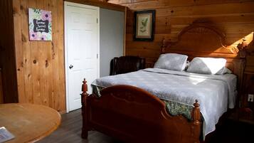 Een houten kamer met een bed, een stoel, een tafeltje en een deur.
