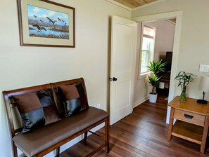 Ein Zimmer mit einer Holzbänkl, einer Tür, einem Blumentopf und einem gerahmten Bild an der Wand.