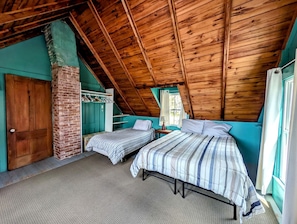 A room with two beds, a brick fireplace, wooden ceiling beams, and a window with curtains. - Scenic Waterfront Summer Cottage with Ocean Views, Kayaking & Beach Access near Bar Harbor, Hancock Point, Maine (Hancock)