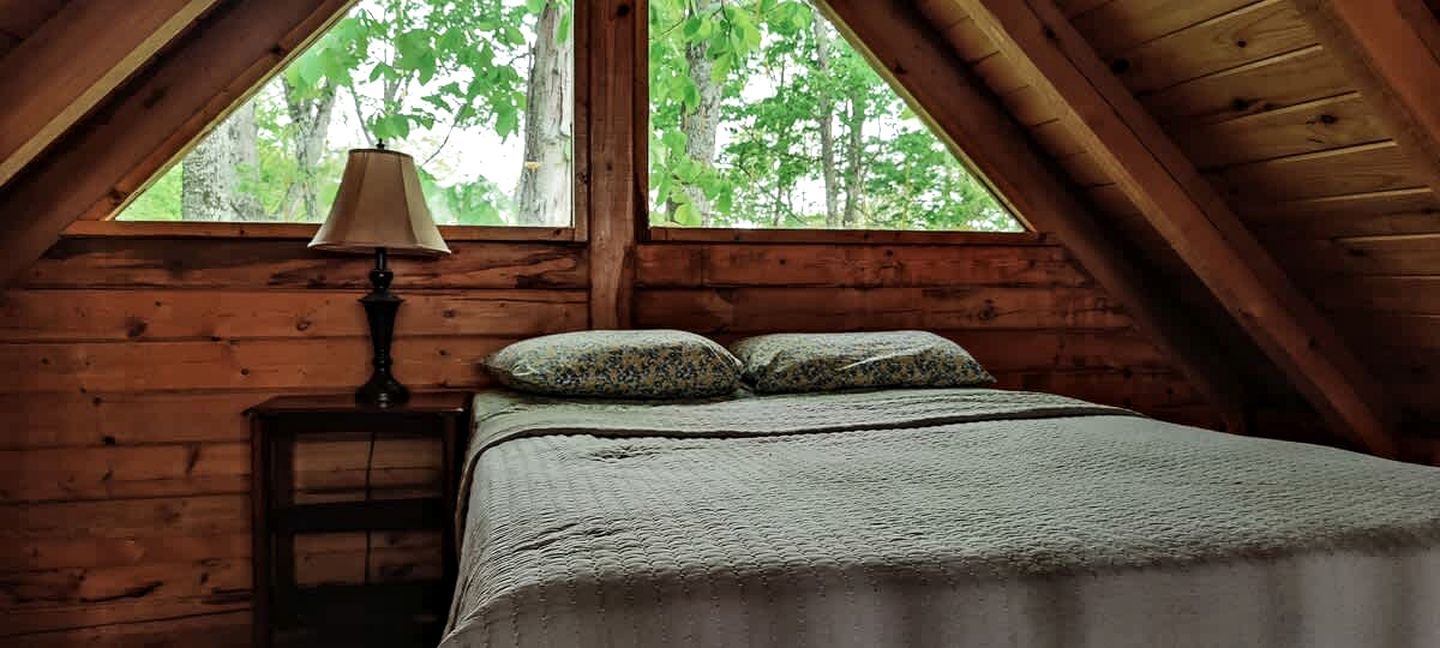 Ein gemütliches Schlafzimmer im Dachgeschoss mit einem Bett, einem Nachttisch und einem Fenster mit Blick auf Bäume.