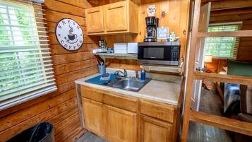 A compact kitchen with wooden cabinets, a coffee machine, a microwave, and a 'Fresh Coffee' sign.