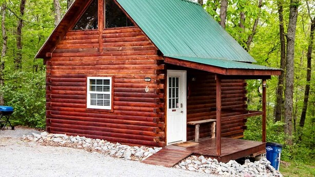 Une cabane en bois avec un toit vert, une porte et un petit porche.