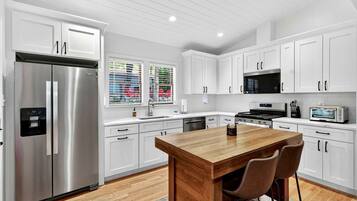 A modern kitchen with white cabinets, stainless steel appliances, a wooden island, and a view of the outside through large windows.