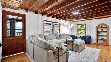 A cozy living room with a sectional sofa, a blue armchair, a wooden bookshelf, and a door with a window.
