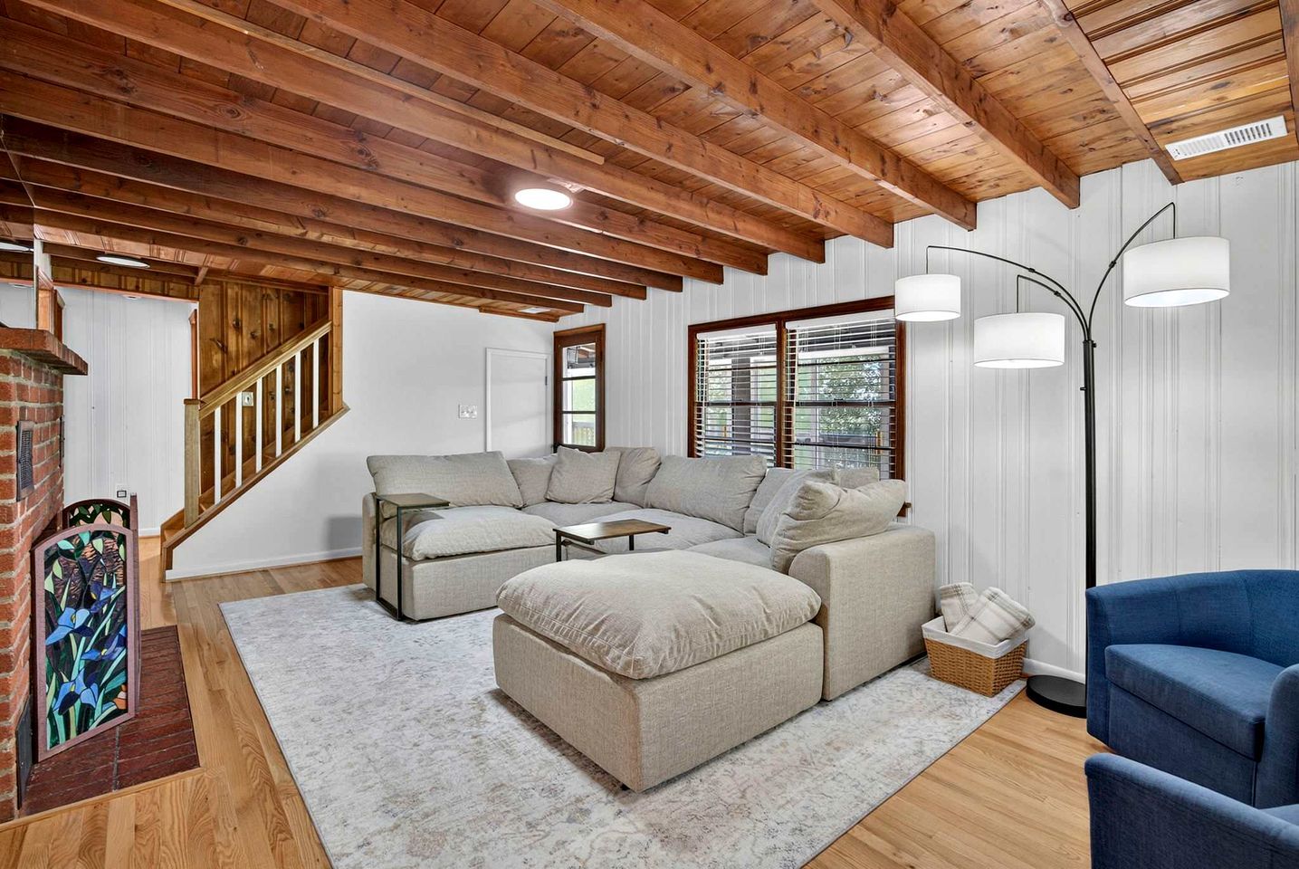 A spacious living area with a wooden ceiling, a sofa set, a blue armchair, and a floor lamp.