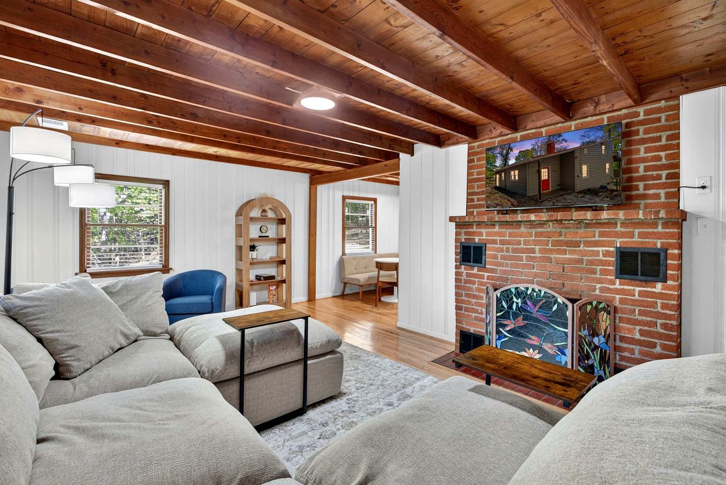Una sala de estar con chimenea de ladrillo, vigas de madera, un sofá, un sillón y una estantería.