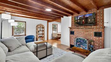 Una sala de estar con chimenea de ladrillo, vigas de madera, un sofá, un sillón y una estantería.