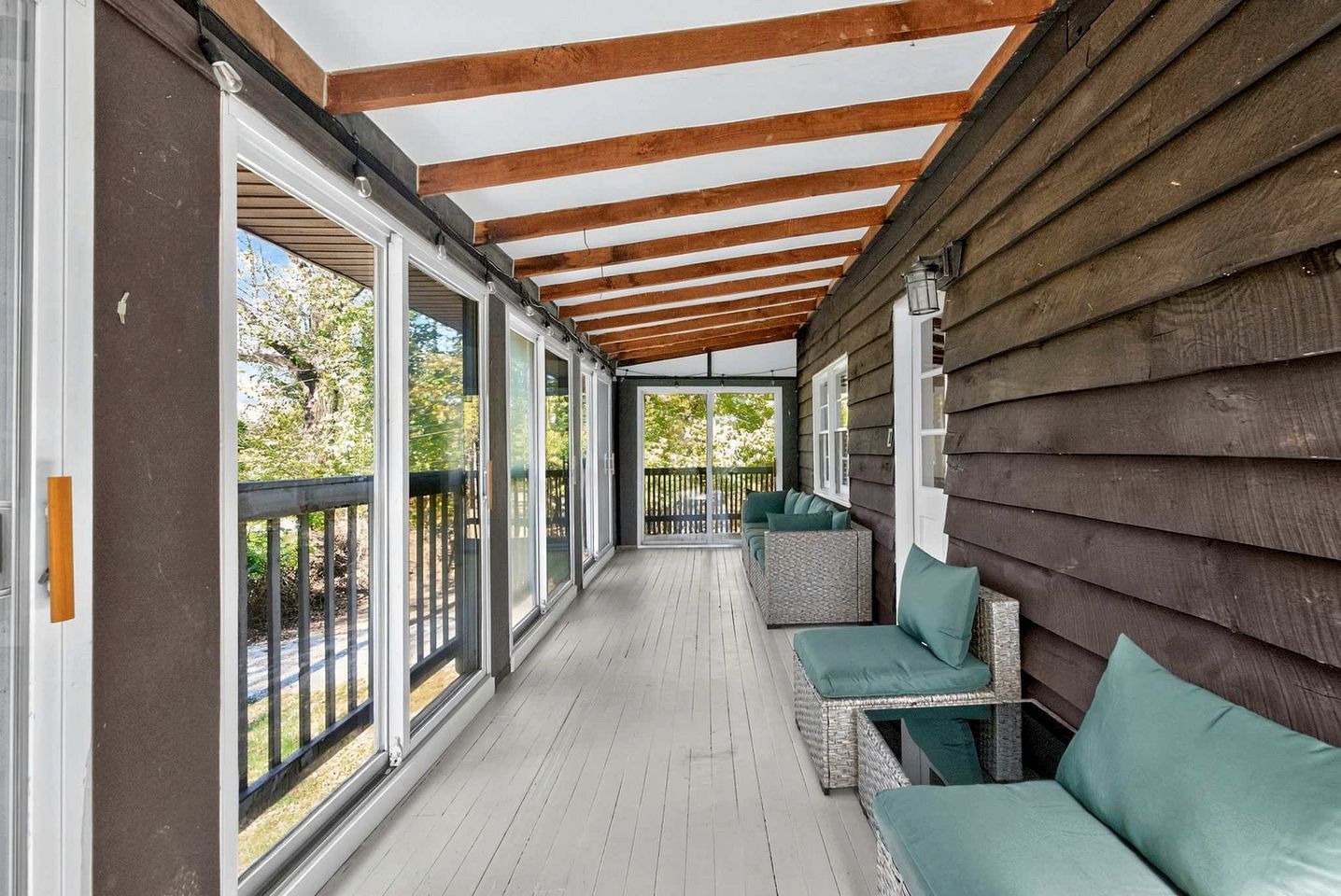 Une véranda couverte avec un plafond en bois, de grandes fenêtres et des sièges d’extérieur.
