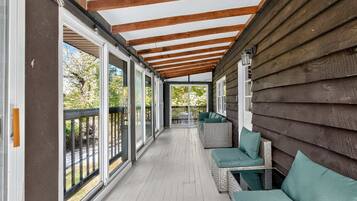 A covered porch with a wooden ceiling, large windows, and outdoor seating.