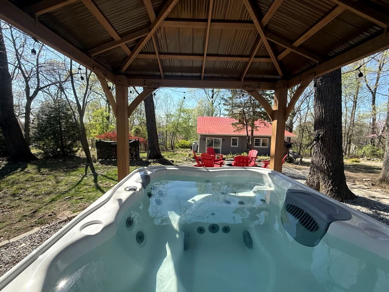A hot tub under a wooden pergola with a house and red chairs in the background.