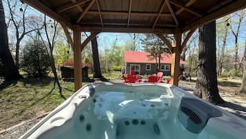 A hot tub under a wooden pergola with a house and red chairs in the background.
