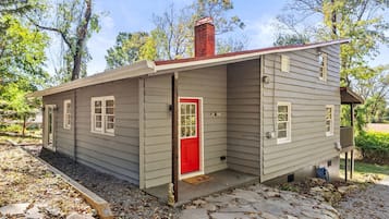 A small, single-story cabin with a red door, a chimney, and a porch.
