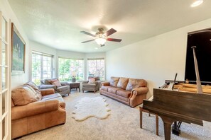 Uma sala de estar com um piano, sofás, uma mesa de centro e um ventilador de teto.