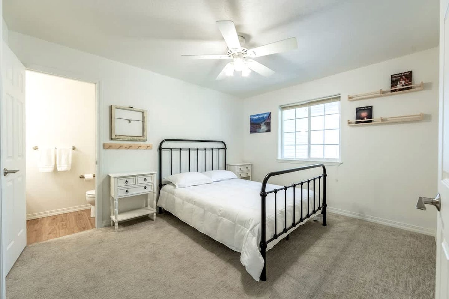 A bedroom with a single bed, a nightstand, a dresser, a ceiling fan, a window, and a door leading to a bathroom.