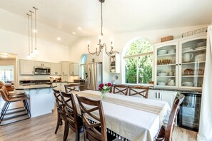 Cozinha moderna com armários brancos, eletrodomésticos de aço inoxidável e uma área de jantar com mesa posta para quatro pessoas.