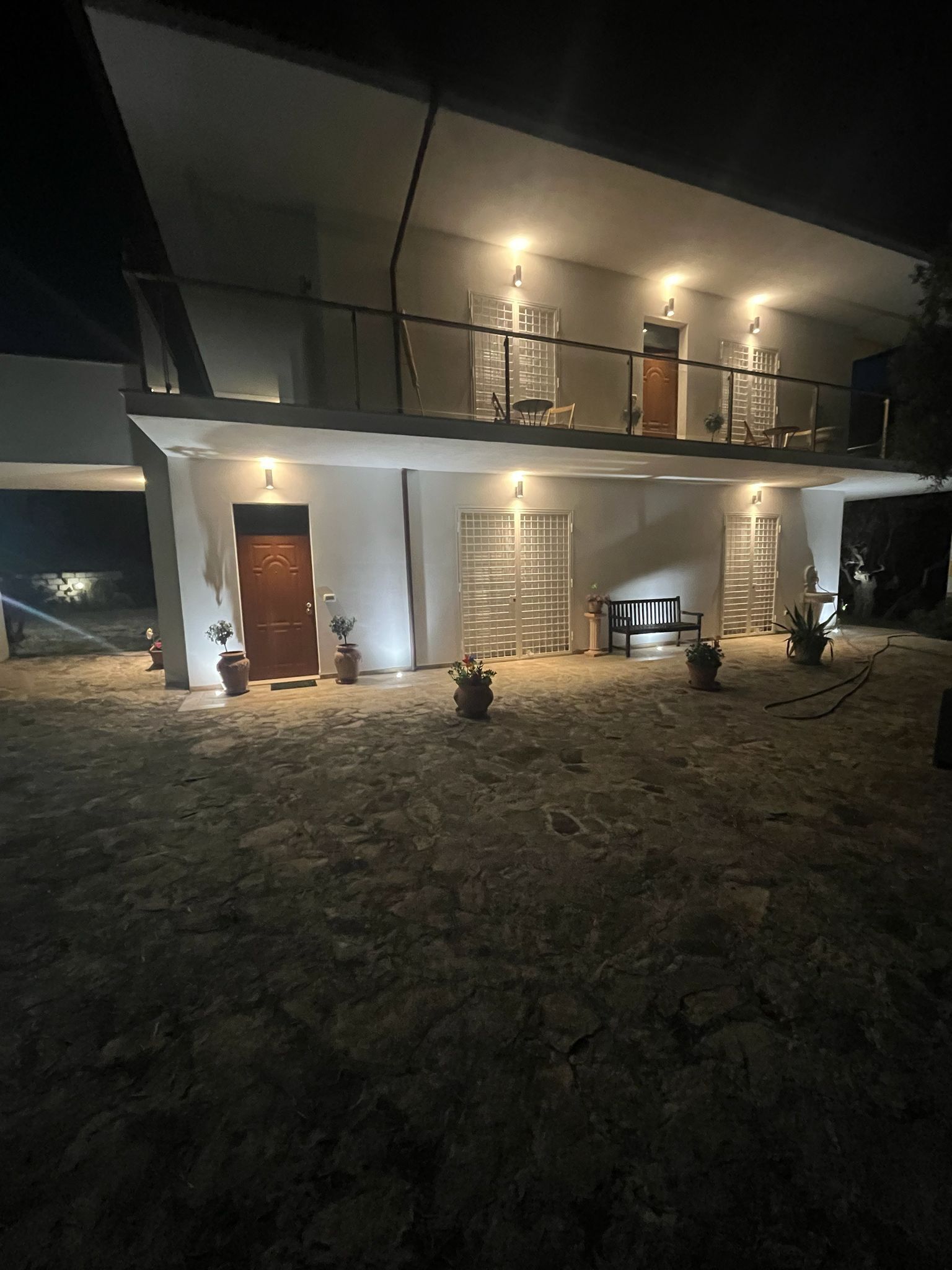 Un edificio de dos pisos con un balcón, varias puertas y plantas en macetas.