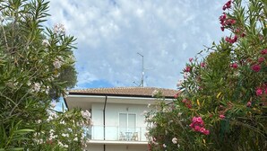 Un edificio de dos pisos con un balcón, plantas en macetas y un camino de grava.