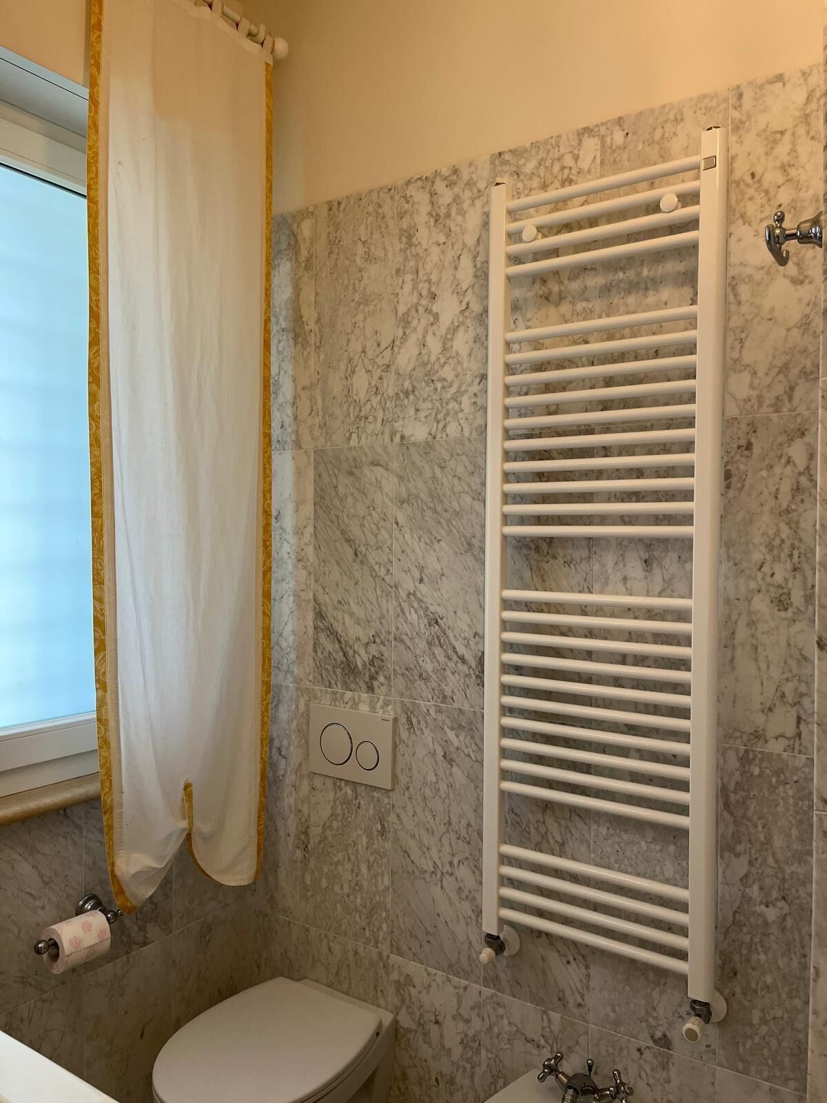 A bathroom with a toilet, a shower curtain, a towel rack, and a marble wall.