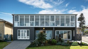 A modern two-story building with large windows, a well-maintained garden, and a clear sky. - Barefoot Beach House (Kiama Downs)