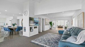 A modern living room with a blue sofa, a dining area with blue chairs, and a kitchen with white cabinets. - Barefoot Beach House (Kiama Downs)