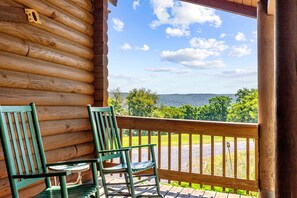 A log cabin with a wooden deck, two green chairs, and a table. - Peaceful Mountain Cabin with Hot Tub, Screened Porch & Views Near Lost River, Baker WV (Baker)