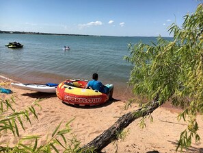 Une plage de sable avec une étendue d’eau, un jet ski, un kayak et une personne assise sur un flotteur gonflable.