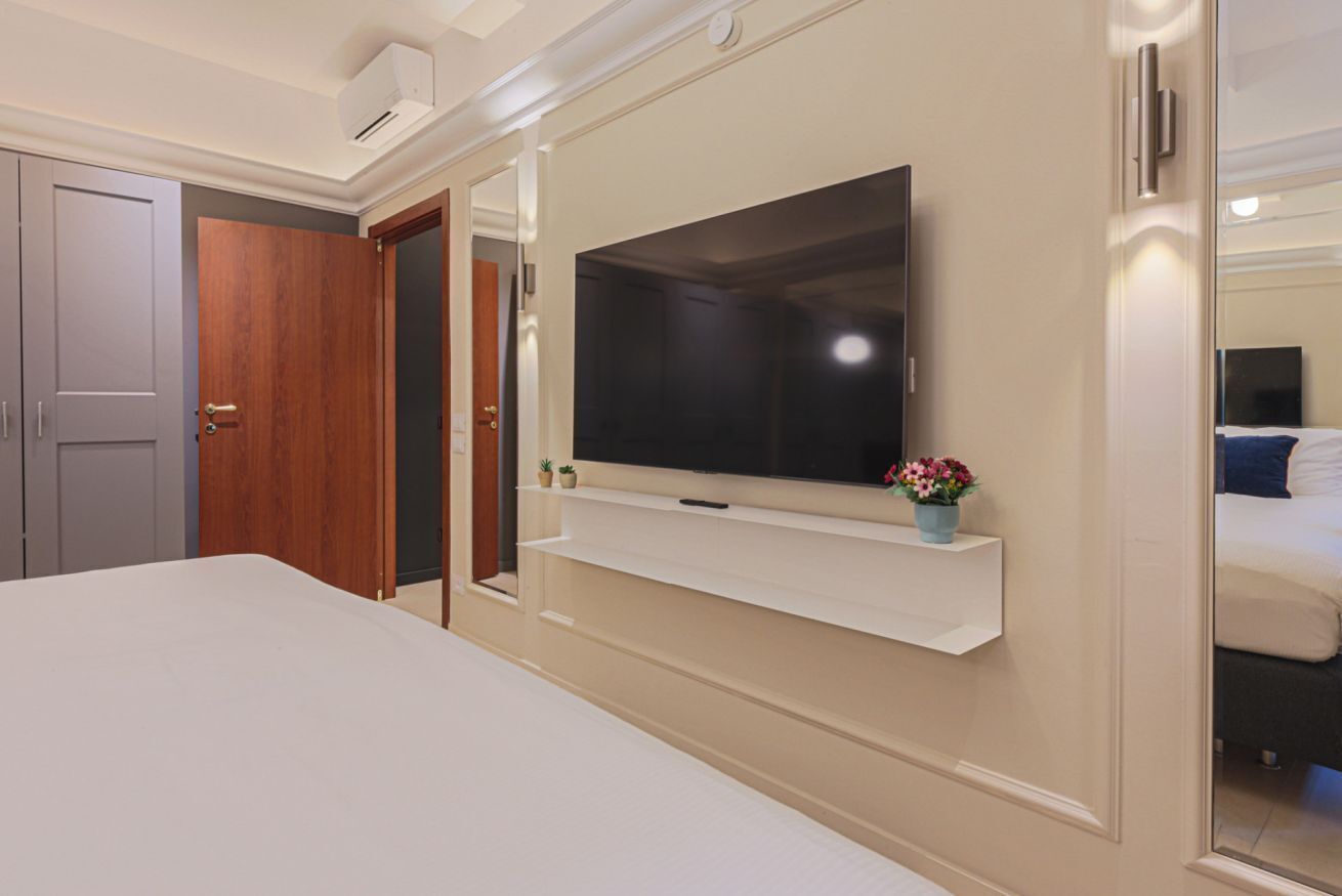 Ein Schlafzimmer mit einem großen Bett, einem Wand-Fernseher, einer kleinen Pflanze und einem Spiegel.