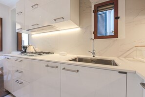 Eine moderne Küche mit weißen Schränken, einer Edelstahlspüle und einem Fenster mit Rollläden.