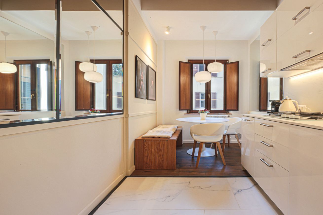 A modern kitchen with a round dining table, white chairs, and pendant lighting.