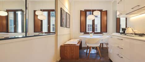 A modern kitchen with a round dining table, white chairs, and pendant lighting.