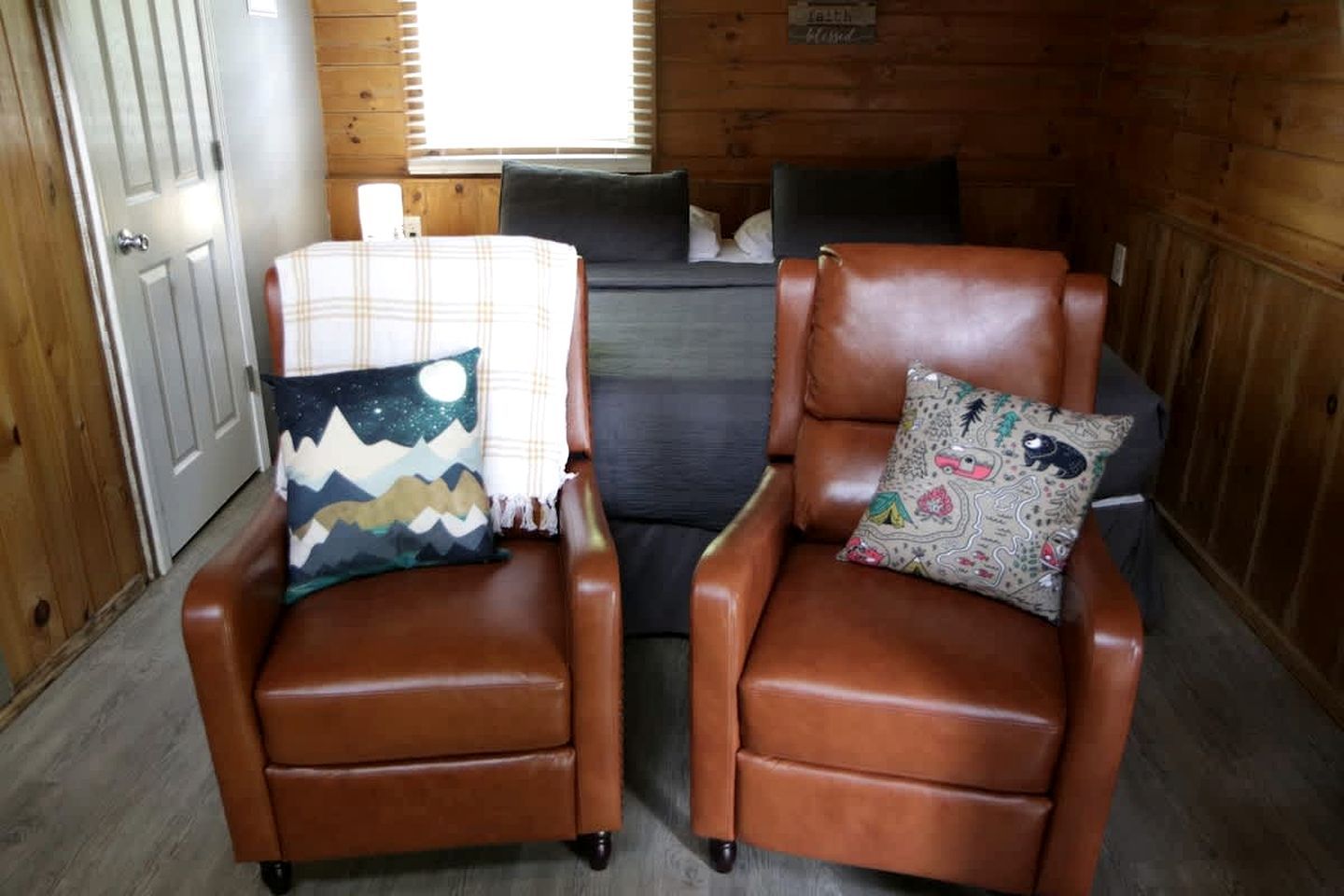 Two brown leather armchairs with patterned cushions, a plaid throw blanket, and a sign on the wall.