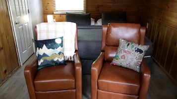 Two brown leather armchairs with patterned cushions, a plaid throw blanket, and a sign on the wall.