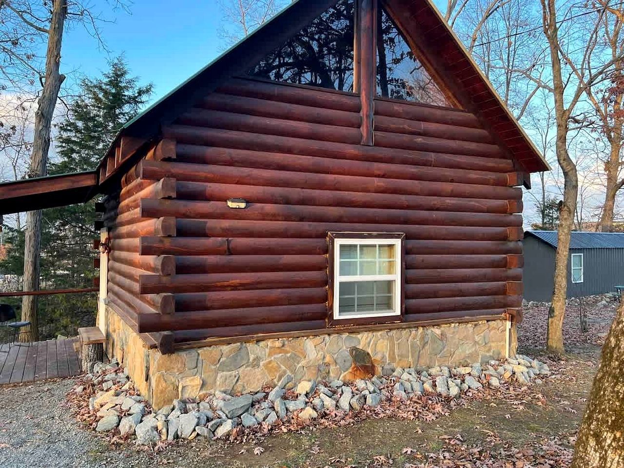 A log cabin with a stone foundation, a small window, and a metal roof.