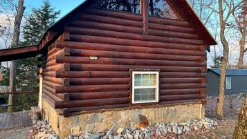A log cabin with a stone foundation, a small window, and a metal roof.