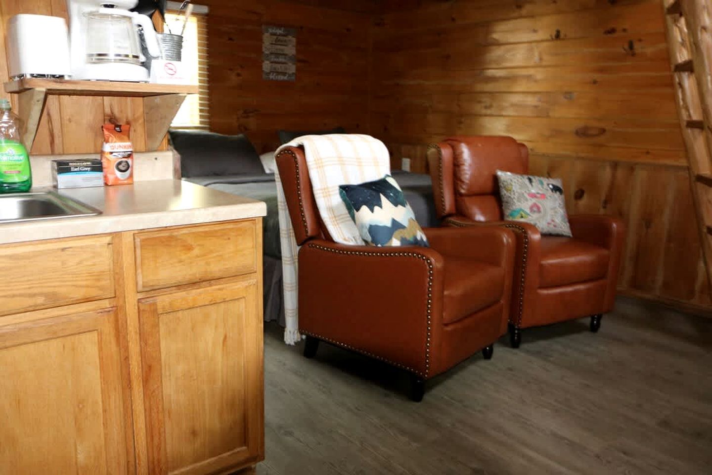 A cabin interior with a kitchenette, a brown leather chair with a pillow, and wooden walls.