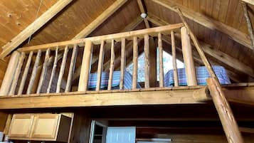 A wooden cabin with a loft bedroom, a kitchen area, and a door leading outside.