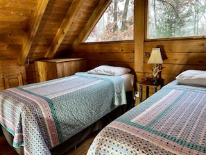 Une cabine avec deux lits, une fenêtre donnant sur la forêt et une lampe sur une table de chevet.