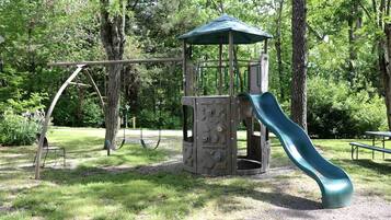 Un parque infantil con tobogán, columpios y una estructura de juegos cubierta.
