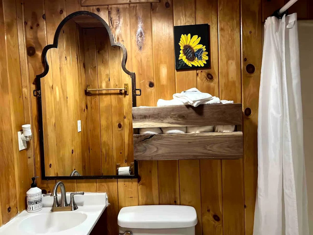 Een houten badkamer met een wastafel, spiegel, toilet en douchegordijn.
