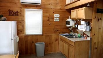 A compact kitchen with wooden walls, a refrigerator, a microwave, and a sink.