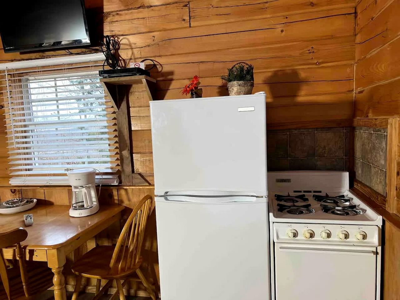 Cocina compacta con refrigerador, estufa y cafetera sobre una mesa de madera.