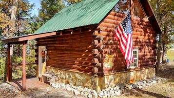A rustic log cabin with a green roof, an American flag, and a welcome sign.